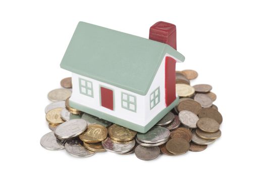 Little house toy on a heap of coins isolated over white background