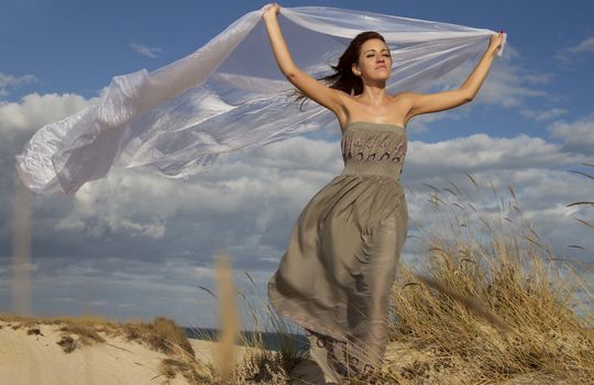 View of a beautiful girl in beach holding a beautiful long white cloth in the wind.