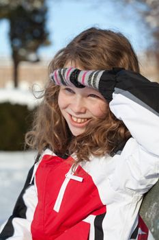 Smiling blond girl in winther cloths sitting on a bench in winter snowy park