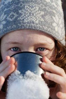 closeup portrait of teenagergirl in winter hat drinking from flask cup
