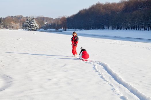 Middle aged woman pulling red sledge with her daughter across a snow field