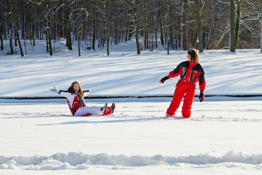 Middle aged woman pulling red sledge with her daughter across a snow field