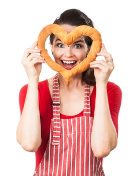 A beautiful happy woman wearing an apron is smiling and peeking through a love heart made out of bread. Isolated on white.