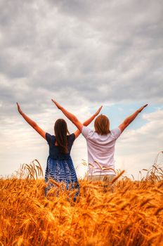 Couple staying with raised hands at a wheat field at sunset time