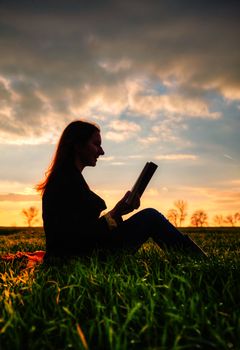  Teen girl reading book outdoors at sunset time