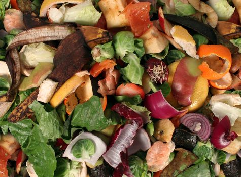 Composting pile of rotting kitchen fruits and vegetable scraps as a banana peel orange and onion garbage waste for recycling as an environmentaly responsible composte that enriches soil in a garden.