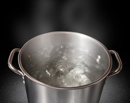 Boiling water in a kitchen pot as a symbol of cooking or food preparation and sterilization of contaminated tap water for healthy pure drinking liquid on a black background.