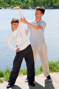 Woman and personal trainer are doing exercises near river