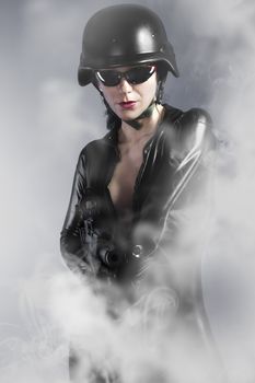 Sexy girl holding gun with helmet over smoke