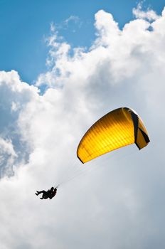Parachuter with instructor descending with a yellow parachute against sky and clouds