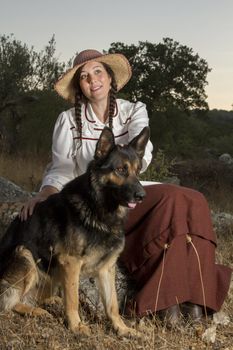 View of a beautiful girl in a classic dress in a countryside set with a dog.