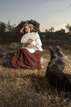 View of a beautiful girl in a classic dress in a countryside set with a dog.