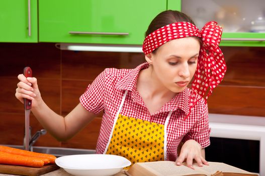 Serious woman in the kitchen with knofe is reading recipe book