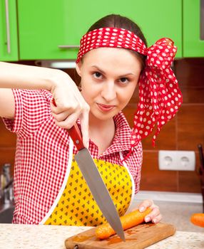 Serious woman in the kitchen is cutting a fresh carrot