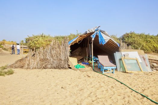 Horizontal landscape two men walking away after a days work at a beach work and repair shop. Generic tropical image with sandy beach and clear blue sky, shot location, Goa India