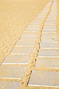 Generic Vertical take of stone flags laid to form a path from a parking lot to a beach over the hot mid day sand