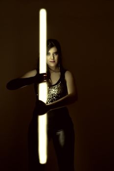 View of a beautiful girl in dark leather clothes holding a light tube.