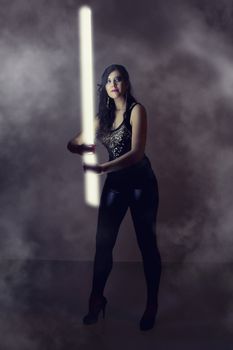 View of a beautiful girl in dark leather clothes holding a light tube.