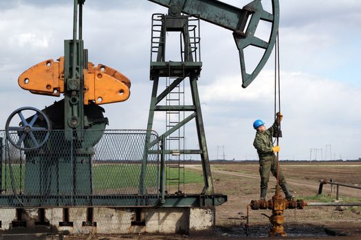 oil worker standing at pipeline and check pump jack