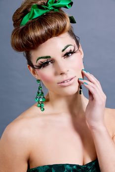 brunette woman with green jewelery and accssesoires on grey background