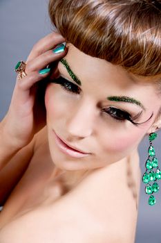 brunette woman with green jewelery and accssesoires on grey background
