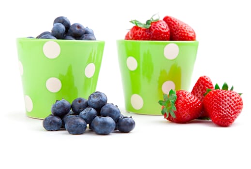 Assorted fresh picked berries in a green mug over a white background. Vertical format with reflection.