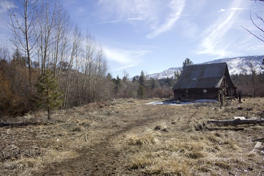 A barn in a meadow with mountains in the back with snow