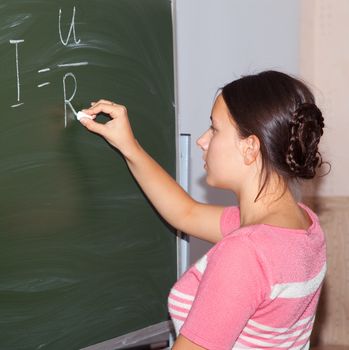 Girl in physics class writing formulas on a blackboard