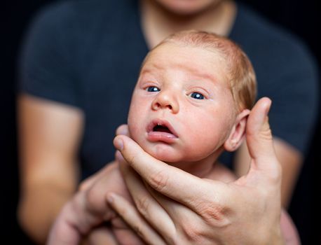 A Mother and Father hold newborn baby in their hands.