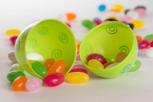 Decorated plastic Easter egg open with colorful jelly beans out of focus in background. Isolated on white background  with light shadow