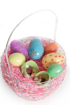 Decorated Easter eggs in Easter basket with jelly beans and pink decorative grass.  Isolated on white background.