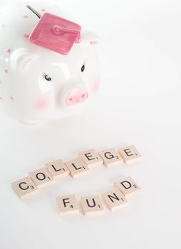 "College Fund" concept. Scrabble letters spell out "College Fund" with out of focus piggy bank with graduation cap in background. Isolated on white background.