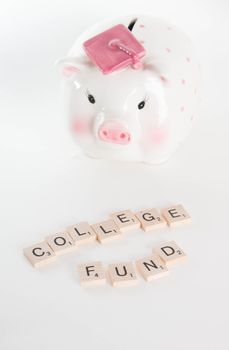 "College Fund" concept. Scrabble letters spell out "College Fund" with out of focus piggy bank with graduation cap in background. Isolated on white background.