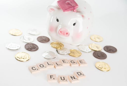 "College Fund" concept. Scrabble letters spell out "College Fund" with out of focus piggy bank with graduation cap and coins in background. Isolated on white background.