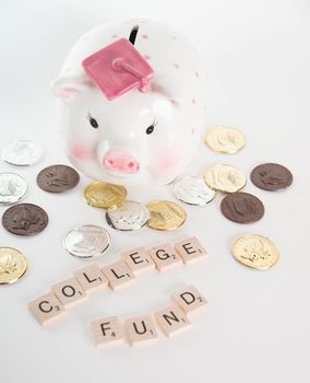 "College Fund" concept. Scrabble letters spell out "College Fund" with out of focus piggy bank with graduation cap and coins in background. Isolated on white background.