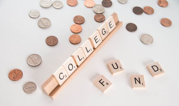 "College Fund" concept. Scrabble letters spell out "College Fund" with out of focus coins in background. Isolated on white background.