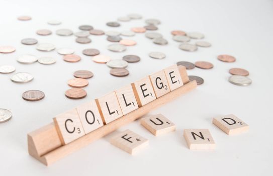 "College Fund" concept. Scrabble letters spell out "College Fund" with out of focus coins in background. Isolated on white background.