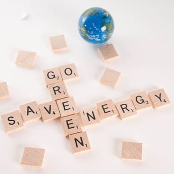 "Save Energy, Go Green" concept spelled in Scrabble letters with out of focus world globe in the background. Isolated on white background