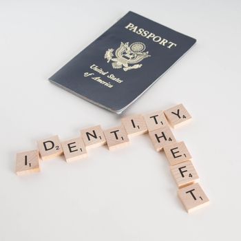 Identity theft spelled in Scrabble letters with US passport out of focus in the background. Isolated on white background.