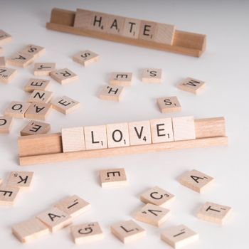 Wooden Scrabble letters spelling out "Love" and "Hate".  "Hate" in background out of focus.  Isolated on white background.