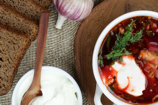 Ukrainian National Traditional Soup with Beet, Vegetables and Meat. Top View of Borscht with Brown Bread, Garlic and Sour Cream on Wooden Plate with Wooden Spoon