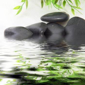 Black basalt spa stones used in hot stone massage immersed in rippling water with overhead bamboo leaves reflected on the surface, conceptual of alternative spa treatments and tranquillity