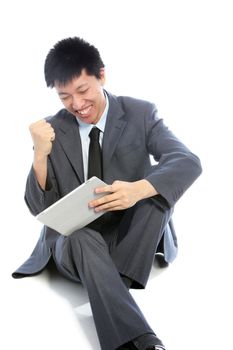 Asian businessman celebrating clenching his fist in the air and smiling happily as he reads some positive information on his tablet