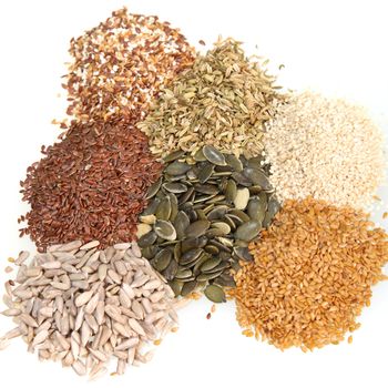 Overhead view of an assortment of fresh dried seeds used as ingredients in cooking including whole and dehusked sunflower, sesame, linseed, legumes and pulses isolated on white