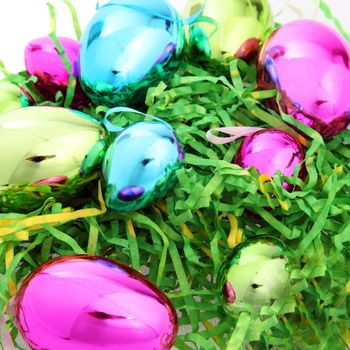 Bright colourful shiny metallic Easter eggs nestling on a bed of green artificial straw