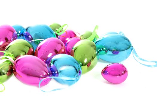 Collection of bright shiny metallic Easter egg ornaments in blue, pink and green on a white background with copyspace