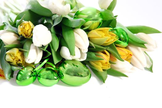 Shiny green metallic Easter eggs nestling amongst the leaves of a bunch of white and yellow spring tulips