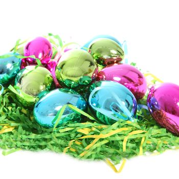 Colourful metallic Easter eggs in pink, blue and green on a bed of green straw isolated on white