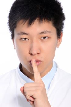 Asian man making a shushing gesture raising his finger to his lips as he asks for silence or for a collaborator to keep a secret with him