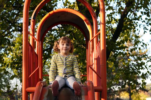 beautiful little girl sitting on playground slide